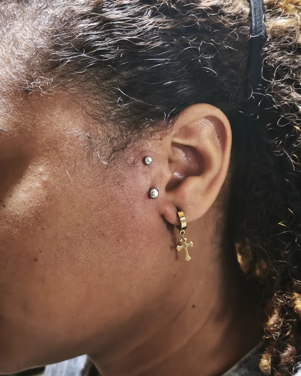 Dos brillantes en el cartílago de la oreja y un arete de cruz en el lóbulo