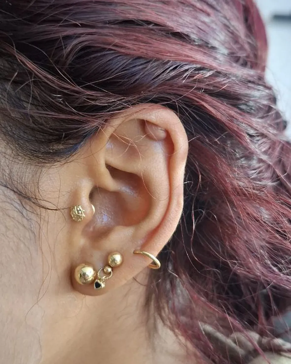 Tres perforaciones con aros y joyas doradas en el lóbulo